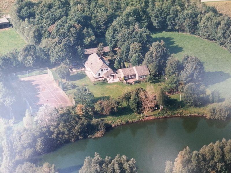 Luchtfoto van het landgoed met het huis, de tennisbaan, de vijver, de weide en het bos